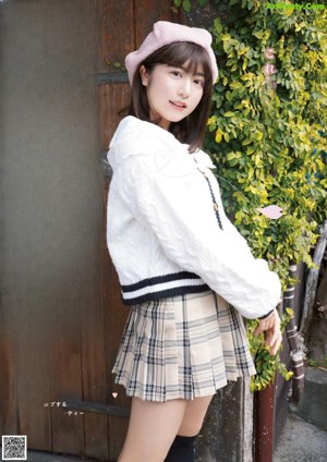 A woman in a white shirt and plaid skirt sitting on a chair.