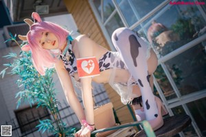A woman with pink hair is sitting on a stool.