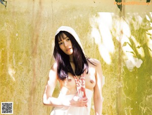 A naked asian woman leaning against a concrete wall.