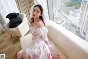 A woman in a white dress sitting on a couch with a pumpkin.