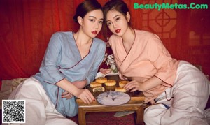 A couple of women sitting on top of a bed.
