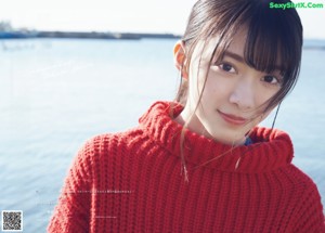 A woman in a red sweater is standing on a concrete wall by the water.