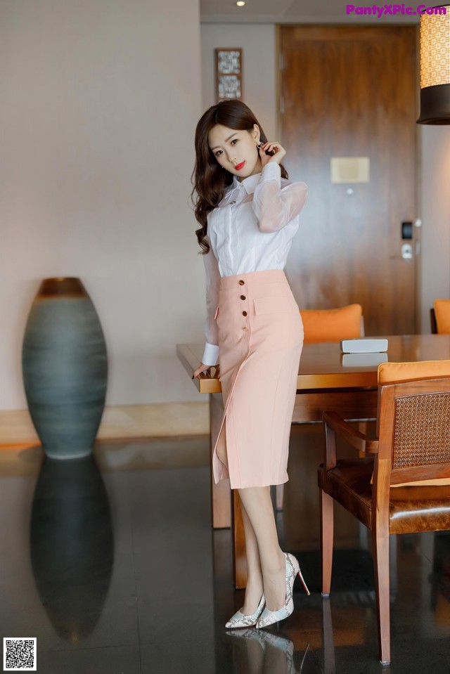 A woman in a white shirt and pink skirt posing for a picture.