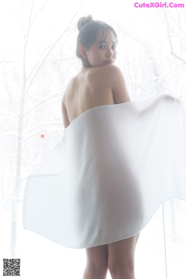 A woman in a white dress standing in front of a window.