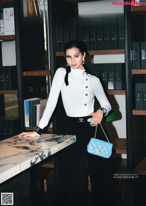 A woman in a gray sweater and red skirt holding a white bag.